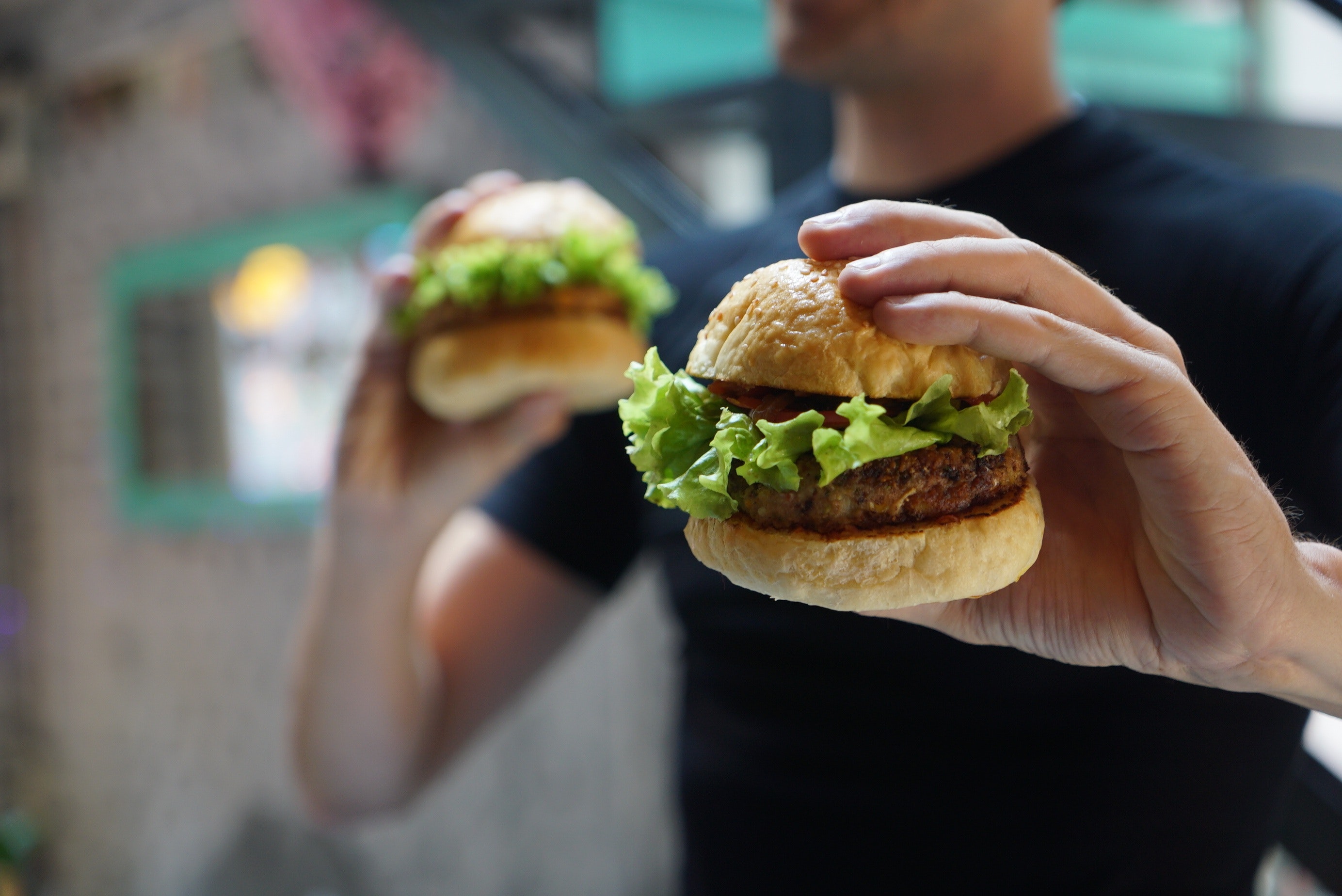 Muž drží v každé ruce jeden hamburger.